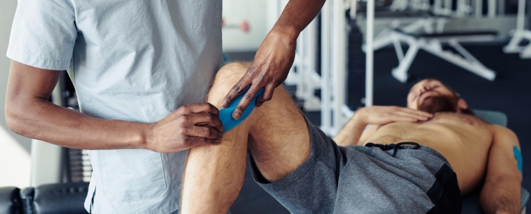 fisioterapeuta a tratar de atleta com lesão desportiva no joelho no gabinete de fisioterapia no desporto